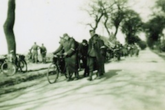 Schwarzweiß Foto: Befreite französische Kriegsgefangene auf dem Weg von Rostock nach Westen. Sie gehen auf einer Allee, einer schiebt ein Fahrrad