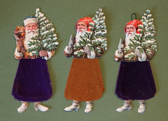 Weihnachtsmänner: im Oberteil und in den Stiefeln als Lackpapier ausgeführt. Sie tragen einen beschneiten Weihnachtsbaum in der Hand. In der einen Ausführung heben sie mahnend den Zeigefinger und in der anderen wird ein Sack mit Äpfeln und Geschenken angedeutet.