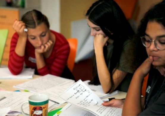 Drei Schüler*innen sitzen an einem Tisch und arbeiten