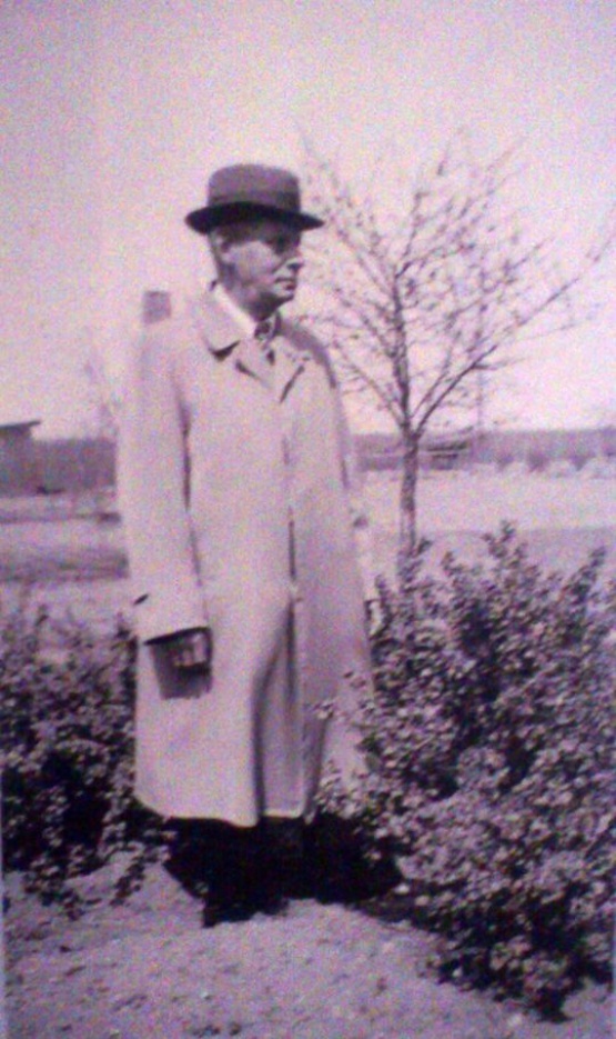 Schwarzweiß Foto mit Blaustich von Alfred Kästel. Er trägt Mantel und Hut, im Hintergrund ein Baum ohne Blätter.