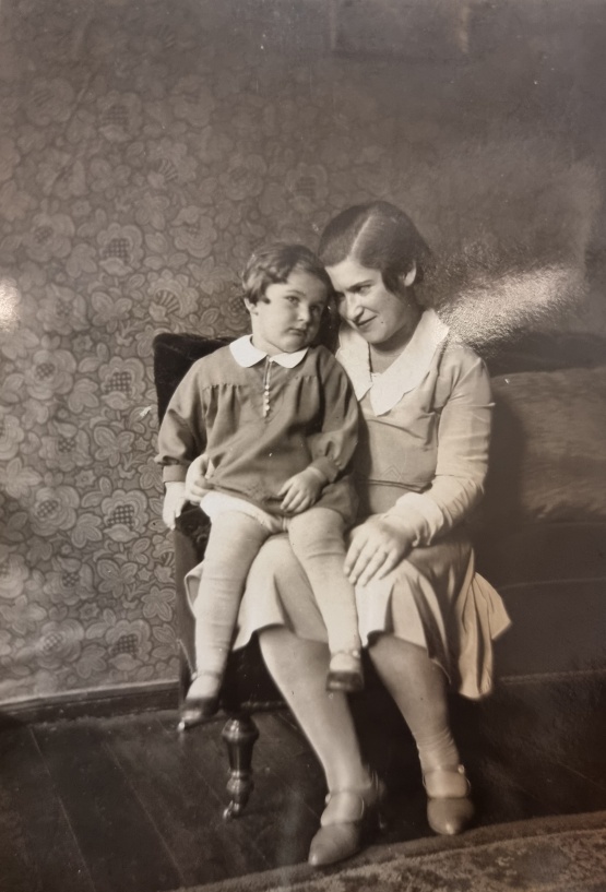 Hella Kohn mit Tochter Jutta, Wismar um 1930. Quelle: Familienarchiv Gottfried. © Quelle: Familienarchiv Gottfried Schwarzweiß Foto: Hella Kohn sitzt auf eine Sofoa, ihre Tochter Jutta sitzt auf ihren Beinen.