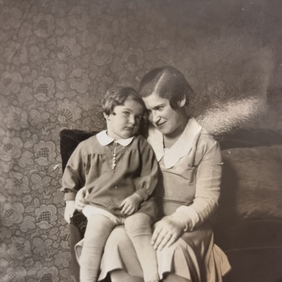 Schwarzweiß Foto: Hella Kohn sitzt auf eine Sofoa, ihre Tochter Jutta sitzt auf ihren Beinen.