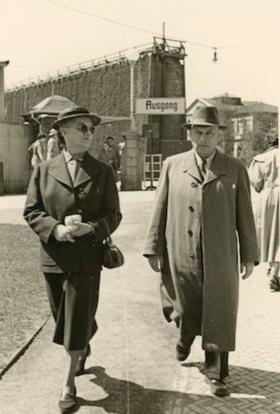 Schwarzweiß Foto einer Straßenszene: Charlotte und Adolf Weingarten im Mai 1954 in Bad Salzuflen. Im Hintergrund ist ein Tor mit dem Schild Ausgang zu erkennen.