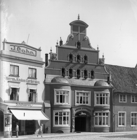 Schwarzweiß Foto, das drei Häuser zeigt. Am Giebel des linken steht "J. Cohn"